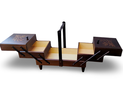 An extra large wooden sewing box with dark walnut color and leaf branch patterns on the lid, equipped with a handle and accordion-style drawers. Fold-out tiered drawers. Fully expanded